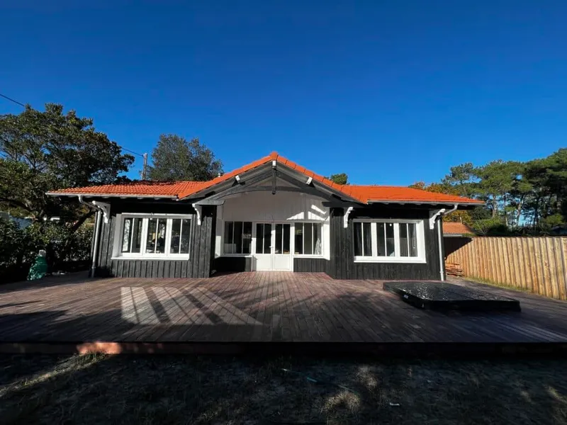 Maison de plain-pied à bardage bois sombre avec une grande terrasse extérieure