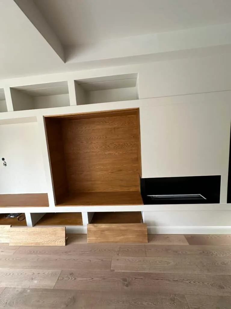 Niche en bois et rangements bas autour de la cheminée intégrée dans un mur blanc
