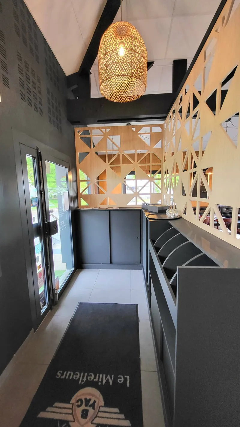 Entrée de restaurant avec claustra géométrique en bois, comptoir sombre et suspension tressée