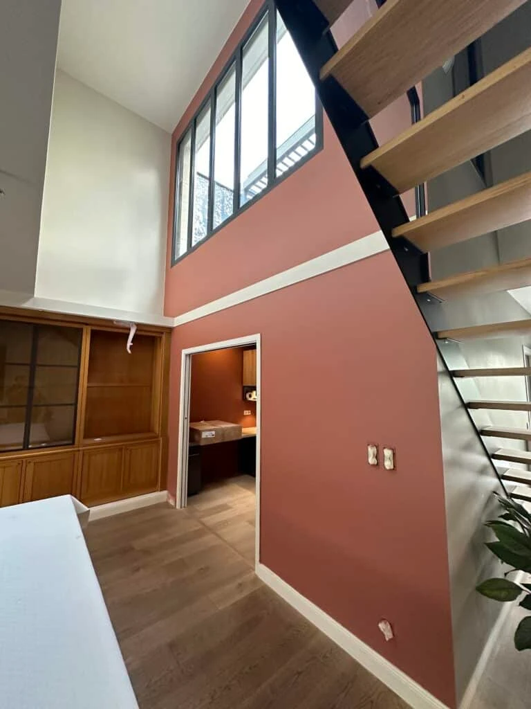 Intérieur avec escalier à limon noir, verrière haute, mur rose poudré et bibliothèque en bois