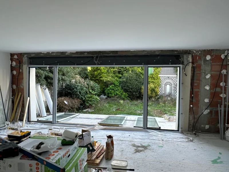 Baie vitrée coulissante installée dans une pièce en rénovation avec murs en briques apparentes