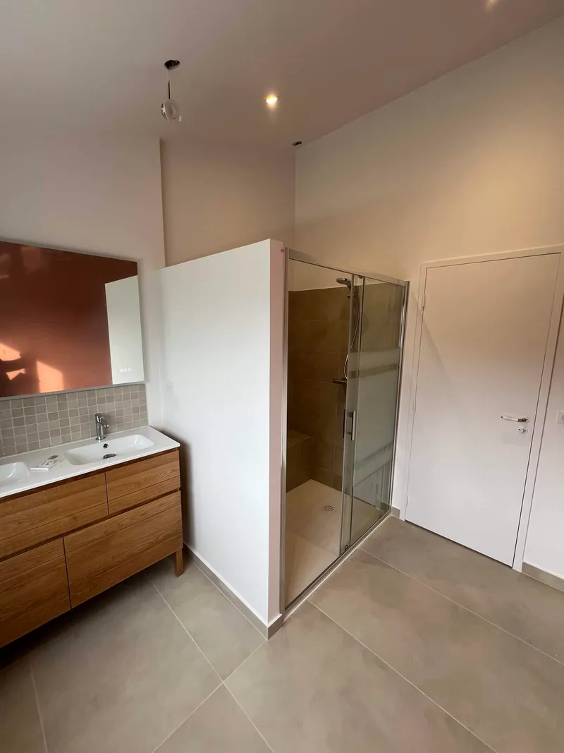 Salle de bains avec douche vitrée, meuble vasque en bois et carrelage beige