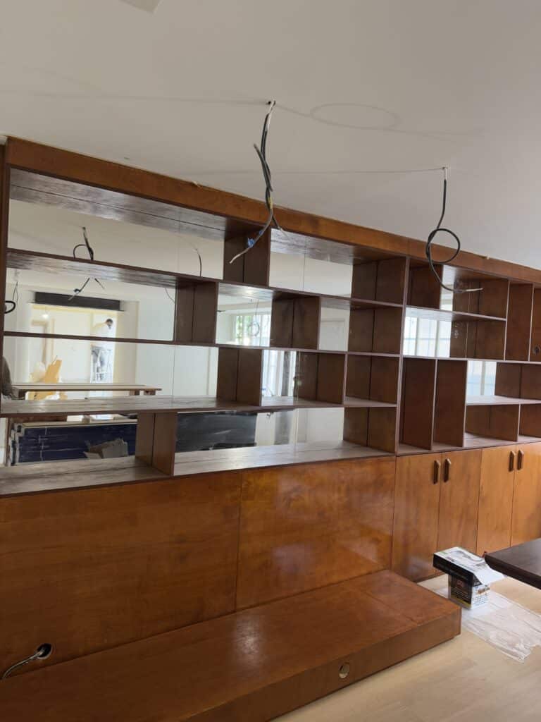 Bibliothèque sur mesure en bois verni, avec étagères ouvertes, armoires basses et miroirs. Fils électriques apparents en rénovation.