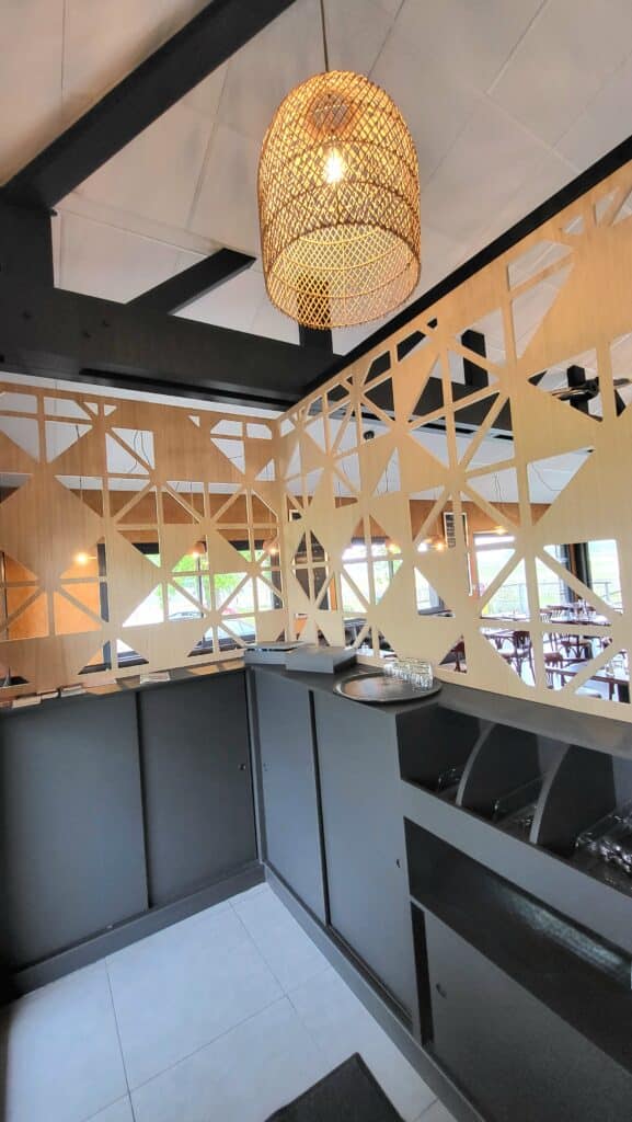Cloison en bois géométrique et luminaire en rotin tressé surplombant un comptoir de service gris. Design intérieur moderne.
