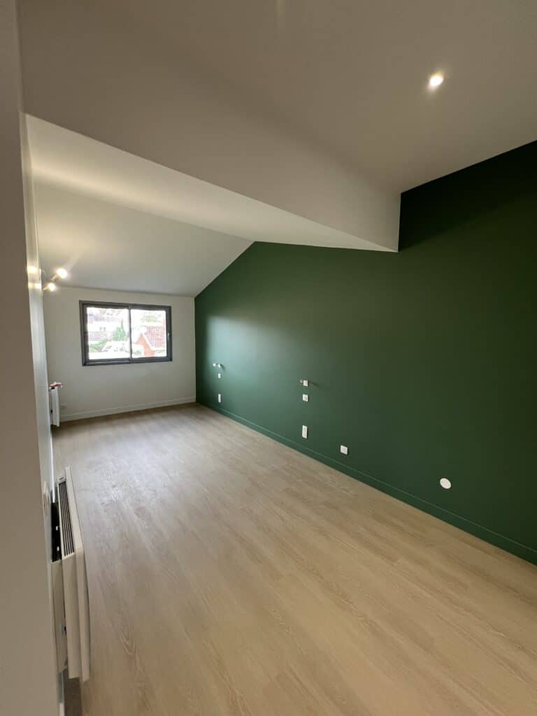 Chambre moderne sous les combles avec mur d'accent vert forêt contrastant avec le parquet bois clair. Architecture épurée et fenêtre.