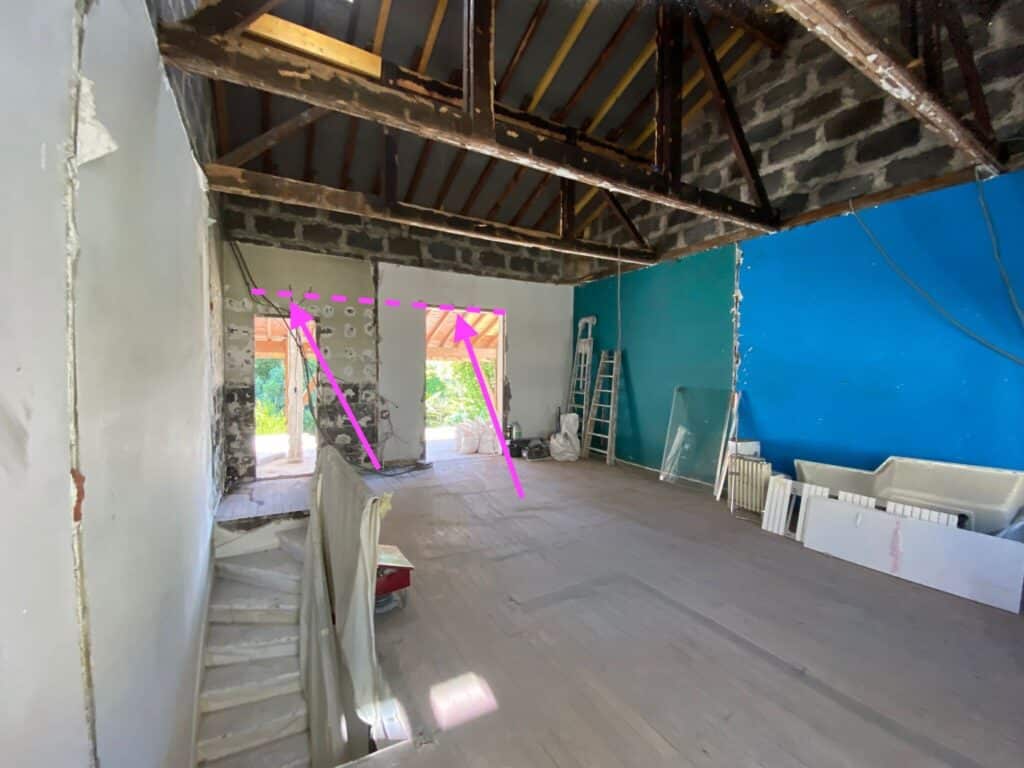 Chantier de rénovation avec démolition des murs pour créer un espace ouvert. Poutres en bois apparentes, sol clair et escalier.