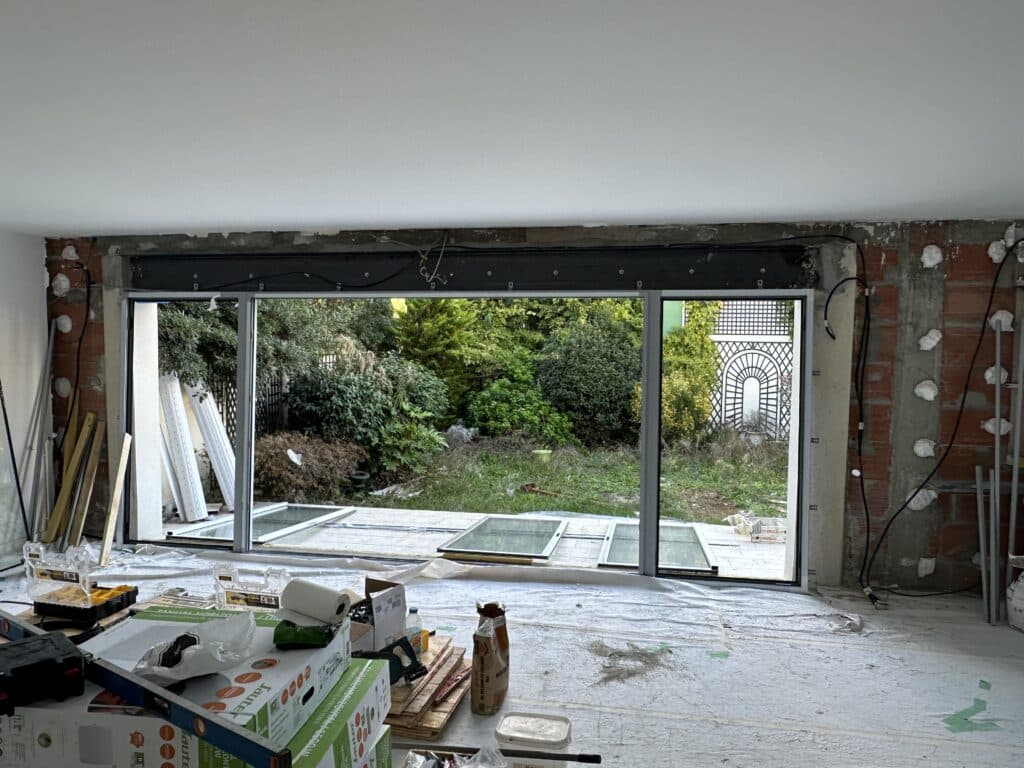 Rénovation : Pose de baie vitrée, lumière et jardin. Chantier de rénovation d'intérieur. Pose de la baie vitrée offrant une grande ouverture sur le jardin. Murs bruts, outils et matériaux au sol.