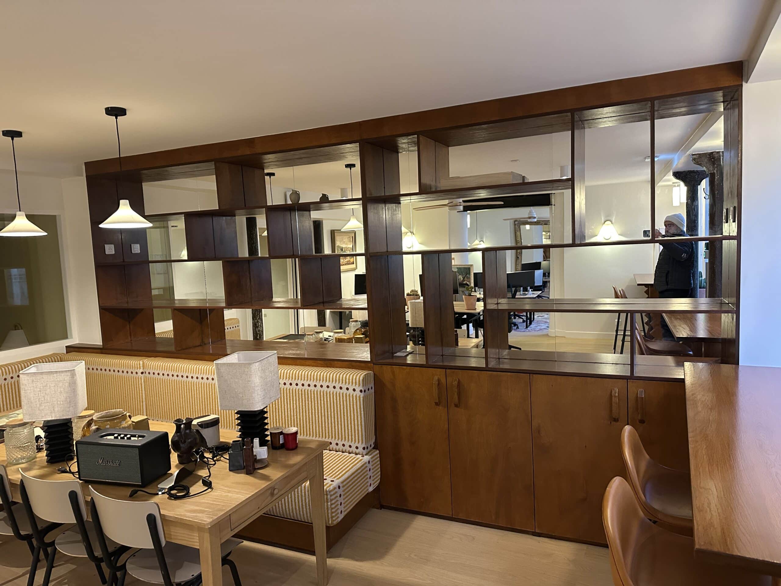Étagères en bois et miroirs, séparation design bureau Séparation design en bois intégrant étagères et rangement bas, face mur de miroirs. Espace repas avec banquette rayée et Marshall speaker.